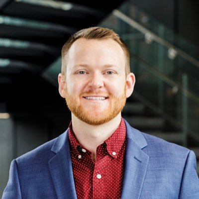 Photo of Associate Director, Ryan Watson, a man wearing a red shirt and blue blazer 